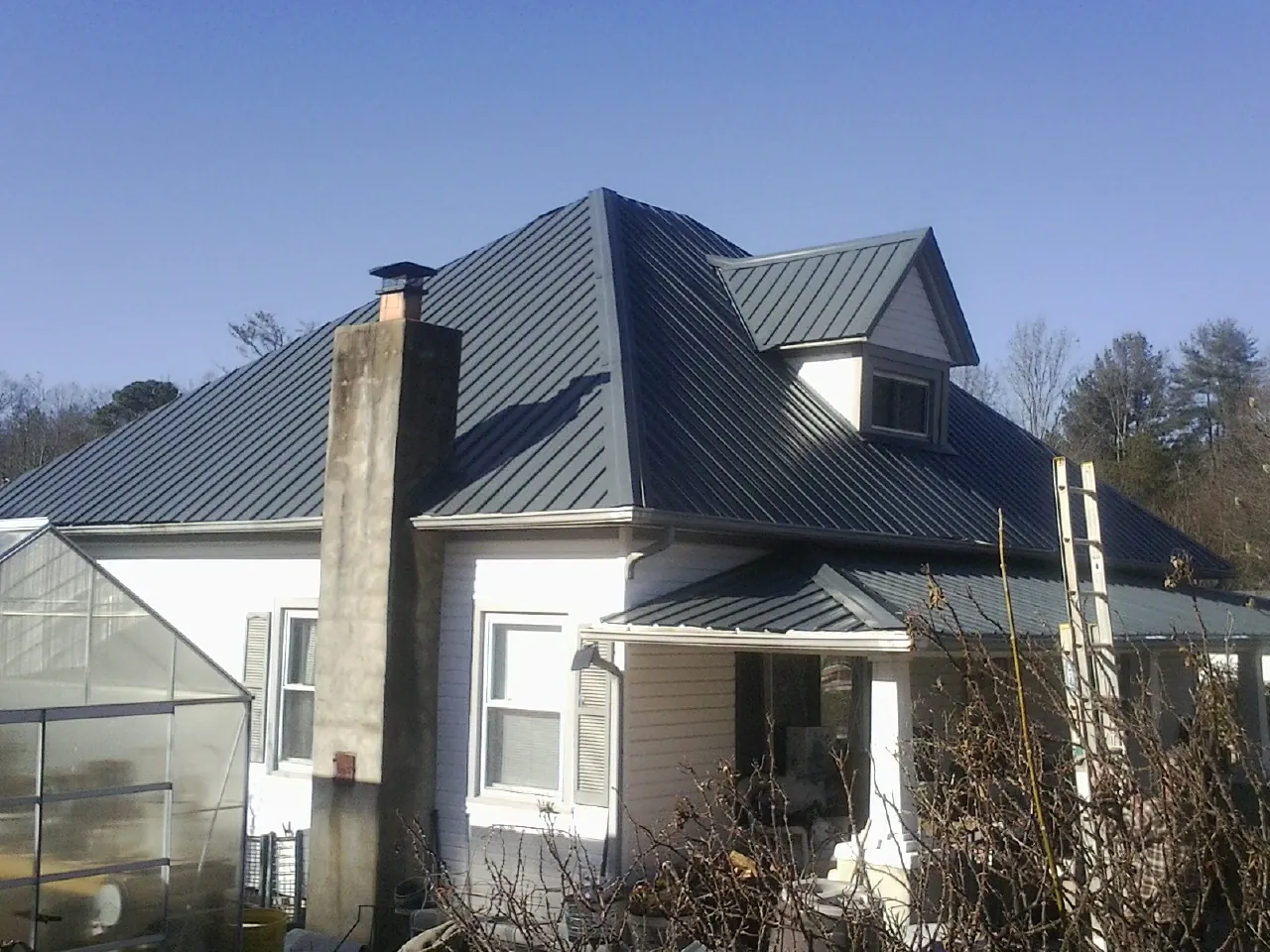 Dark blue standing seam metal roof on a white farmhouse with dormer — Slate & Tile Roof Repair by Roofing Brothers in Onsted