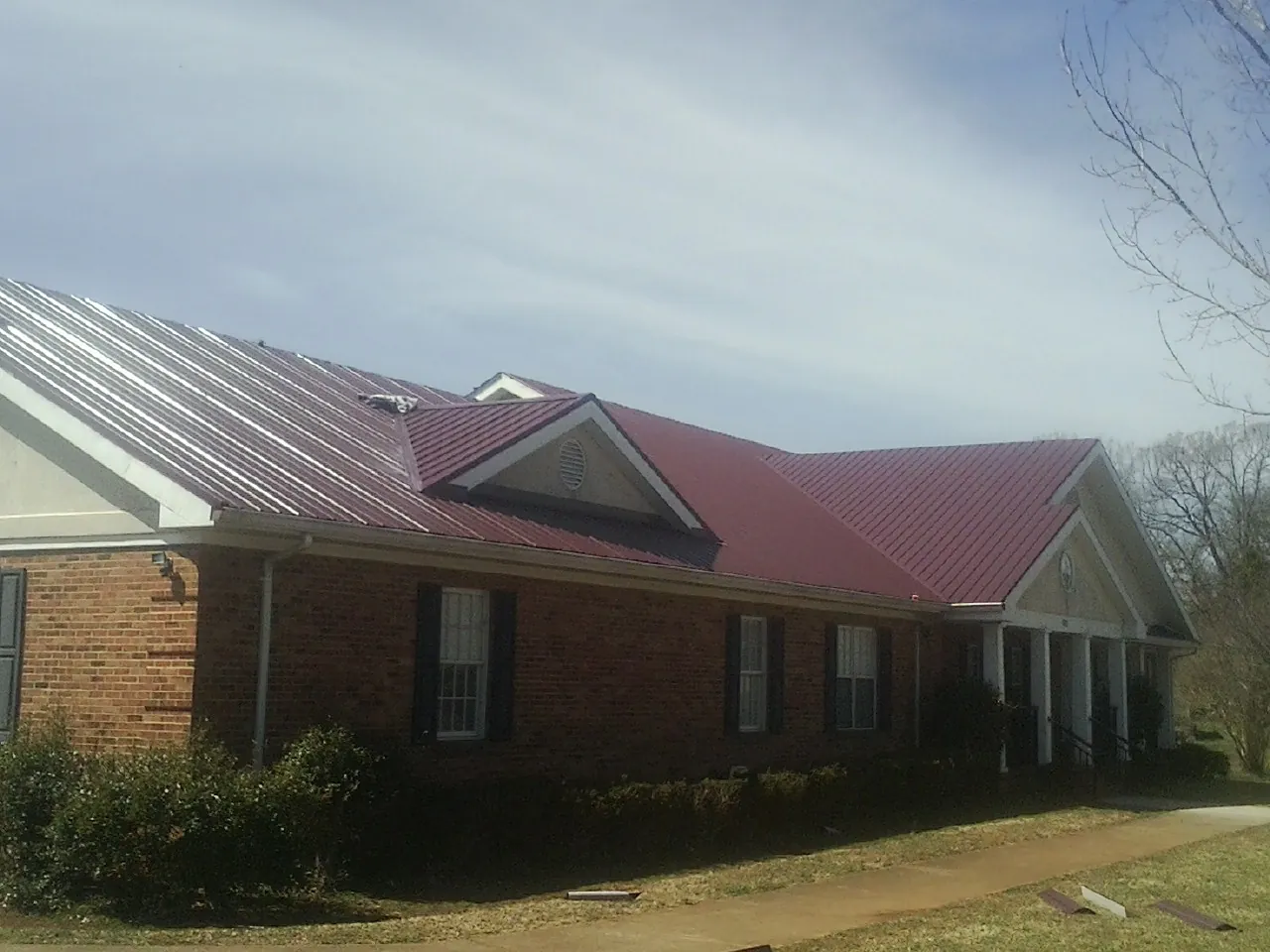 Red metal roof with gabled entries on a long brick building, from a Hail Damage Roof Repair job in Onsted