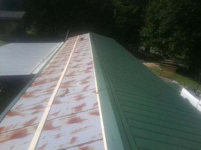 Old rusted panels beside newly installed green metal roofing — Wind Damage Roof Repair by Roofing Brothers in Onsted