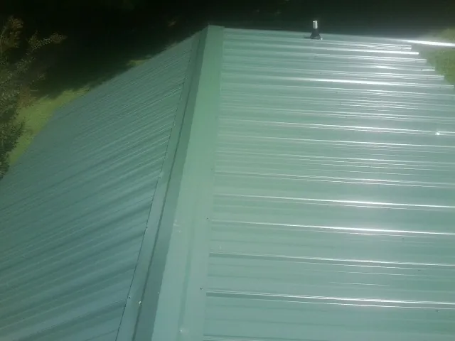 New green metal panels meeting at the ridge of a roof — Flat Roof Repair work by our crew in Onsted
