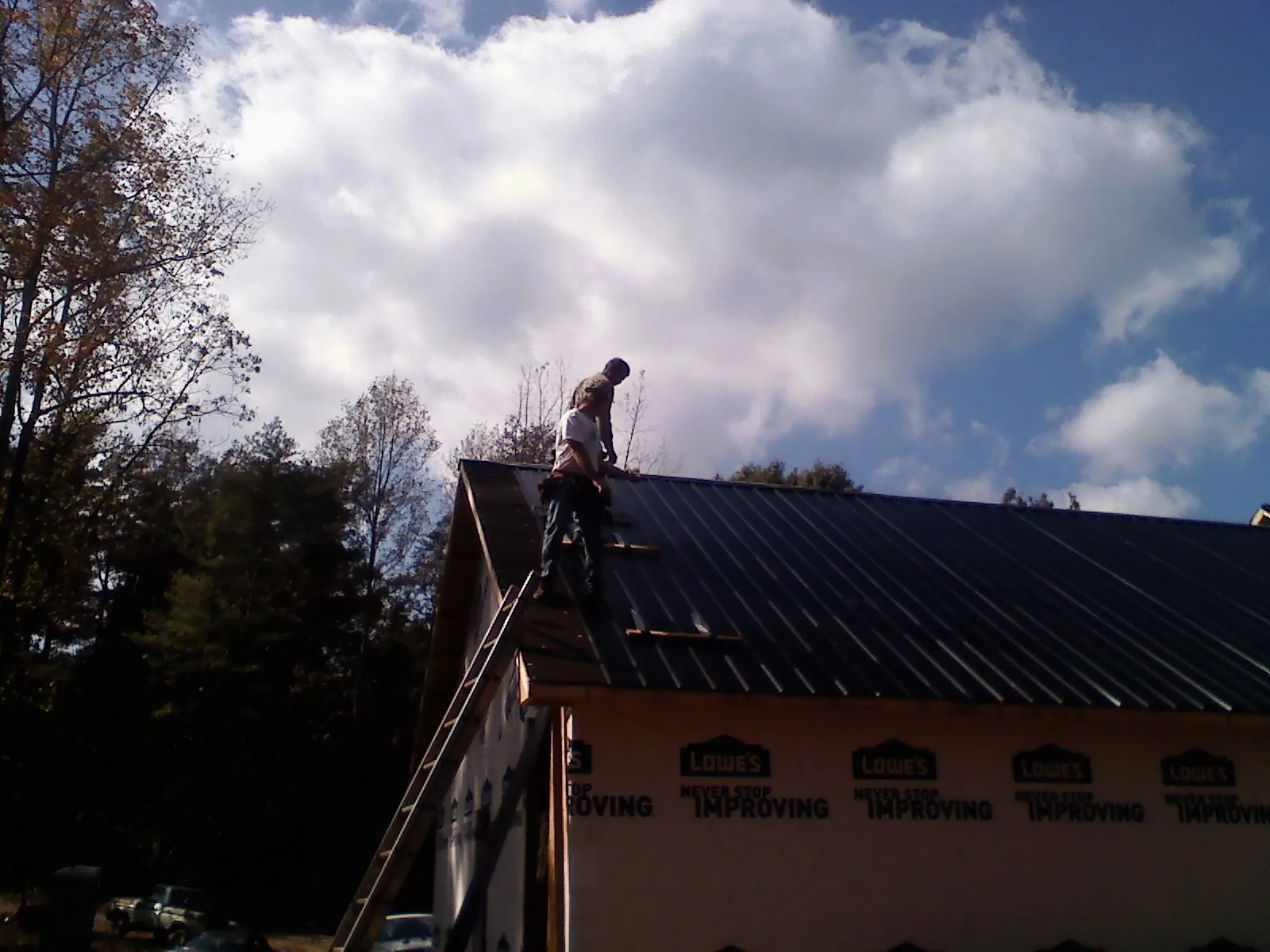 Roofer fastening dark metal panels high against a cloudy sky, from a Roof Inspection job in Onsted