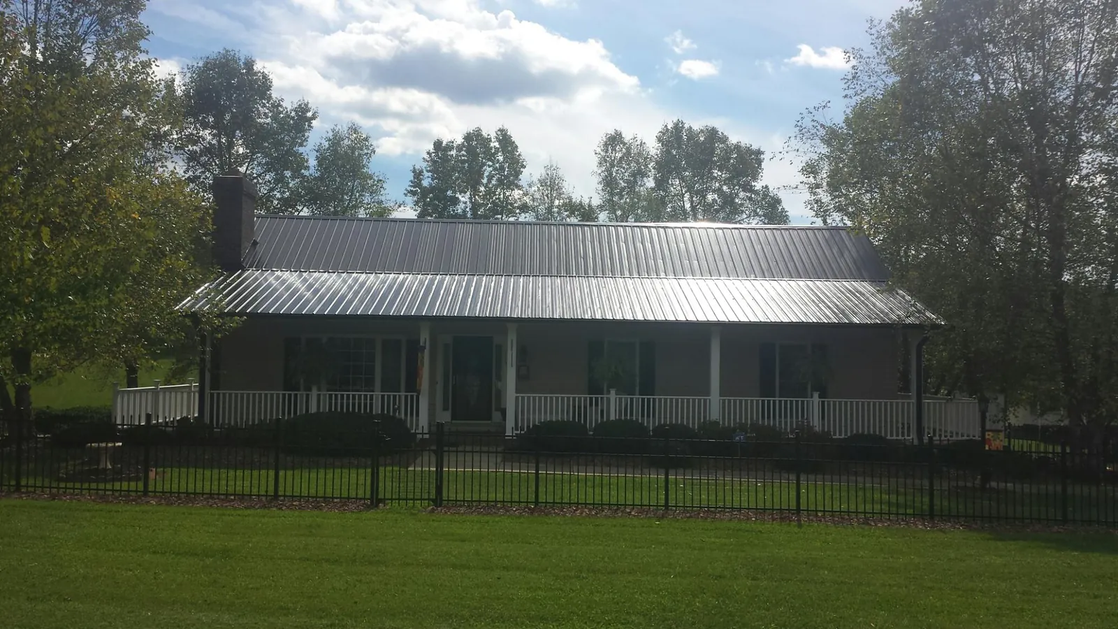 Gray metal roof on a brick ranch with a full width front porch — Gutter Guard Installation work by our crew in Onsted