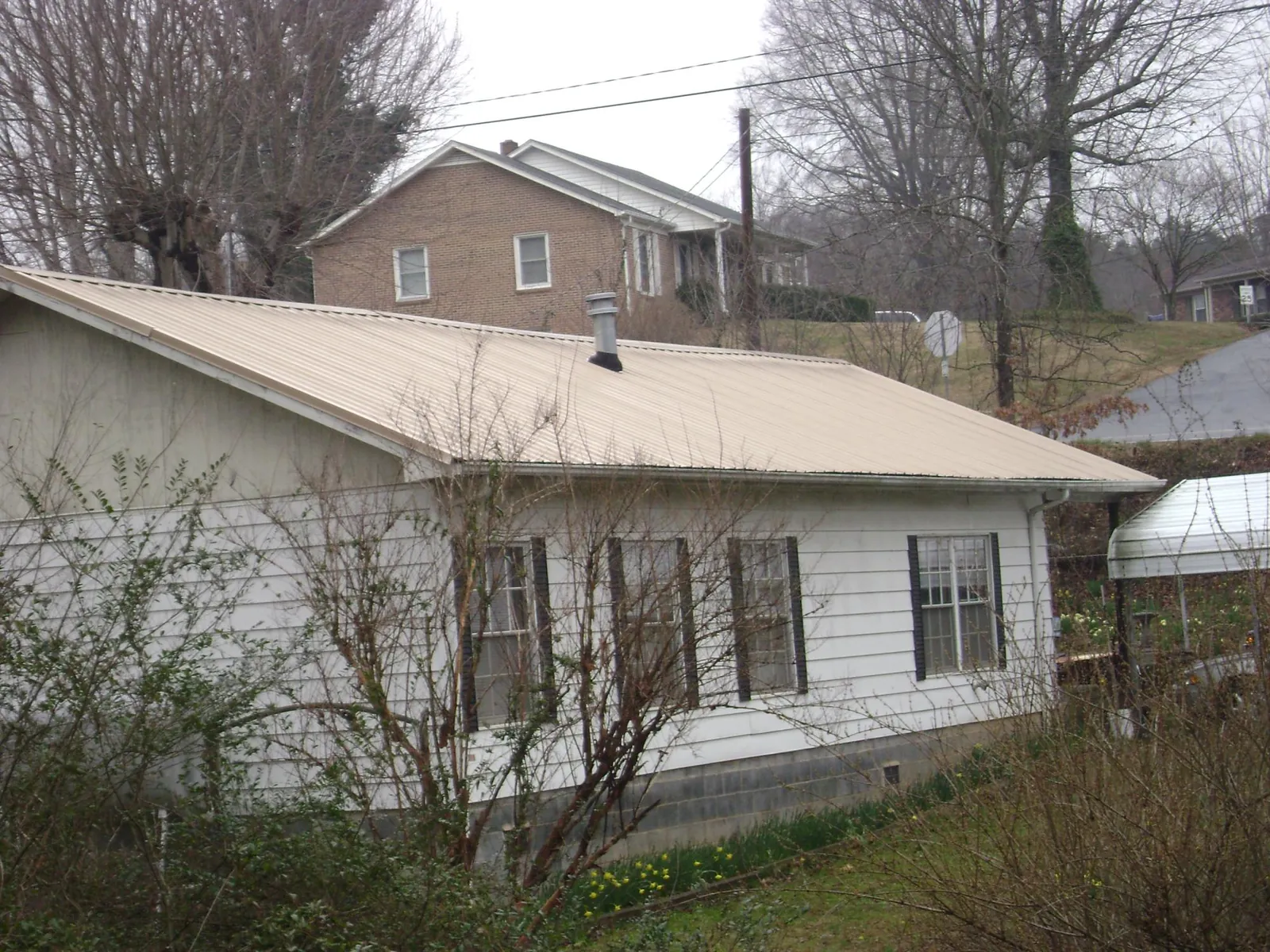 Tan metal roof on a white sided house set into a hillside — Commercial Roofing by Roofing Brothers in Onsted