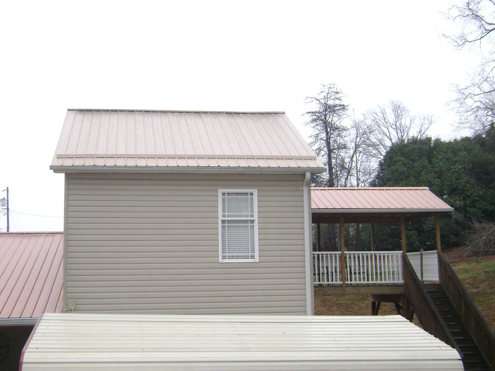 Tan metal roofs on a two story addition and attached porch, from a Roof Replacement job in Onsted